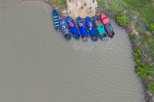 Aerial view of several motorboats docked at a riverbank with people wearing orange life vests standing nearby in Monrovia, Liberia.