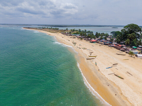 Aerial view of a sandy beach with small wooden fishing boats and a coastal village nestled among trees along the shoreline in Monrovia, Liberia.