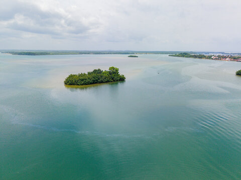 Aerial view of a small, lush green island surrounded by the calm, expansive waters of a lagoon under a cloudy sky near the coast of Monrovia, Liberia.