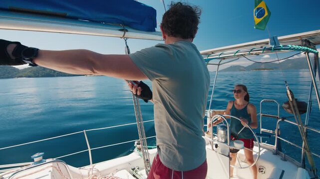 Sailing in the smooth sea during sunny day and navigate with the cellphone. Man and woman sail the small sailing boat in the region of the island of Ilha Grande in Brazil