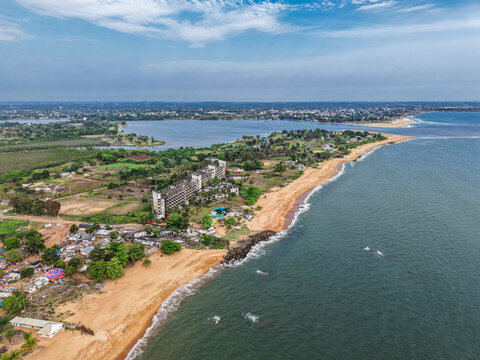 Aerial view of the ruins of the Ducor Hotel on a headland in Monrovia, Liberia, with the Atlantic Ocean coastline, sandy beach, and surrounding urban landscape.
