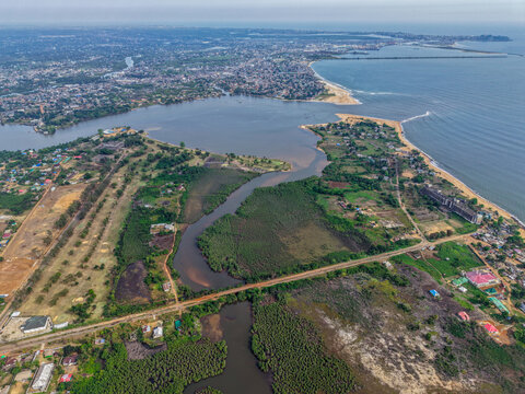 Aerial view of the coastal landscape featuring a winding river flowing into the Atlantic Ocean, lush mangrove forests, and urban development along the shoreline in Monrovia, Liberia.