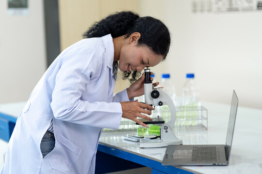 African American female scientist working with microscope and notebook computer in laboratory