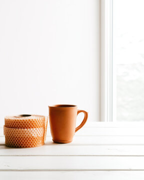 Untreated clay mug and honeycomb paper wrap on white wooden table with bright daylight and clean minimal space for product packaging