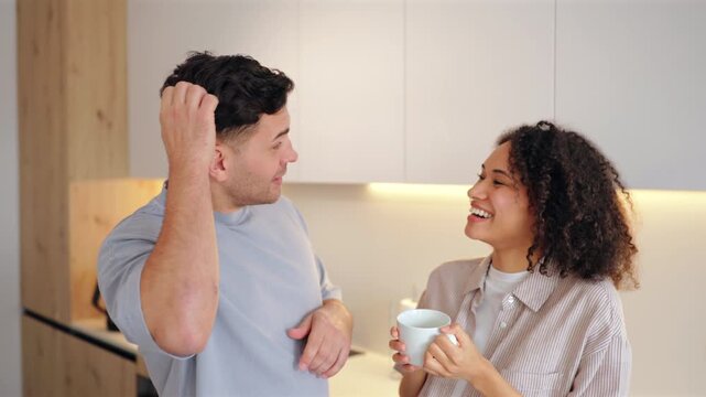 Diverse couple young women and men with coffee in the morning sharing conversation in modern kitchen. Smiling pair enjoys warm drinks while talking and laughing together in cozy home setting.