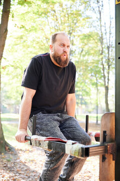 Man trains on parallel bars at outdoor gym in park and exhales with effort. Vertical fitness scene for bodyweight exercise, strength building, endurance, or active lifestyle promotion