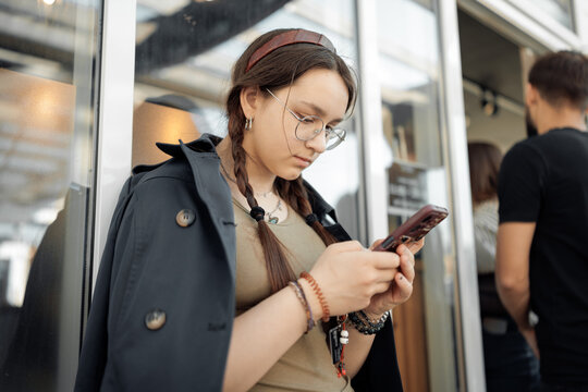 A teenage girl with braids and glasses deeply focused on her