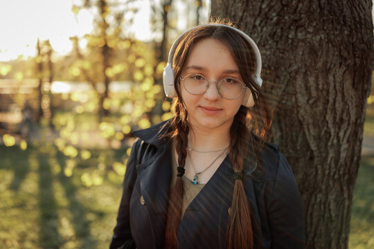 A teenage girl with glasses and braided hair leans against a tree in