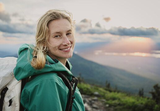 Smiling blonde woman hiking on a mountaintop in Maine at sunset.