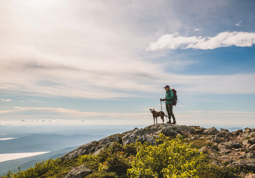 Hiker and dog stand on mountain summit enjoying scenic view, Maine