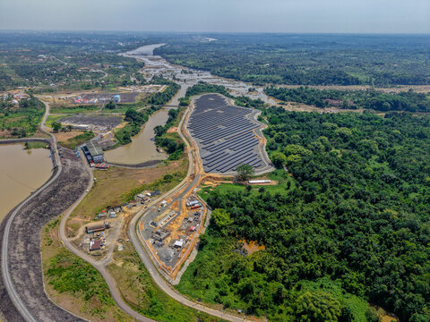 Aerial view of a solar farm with rows of photovoltaic panels situated near a river and reservoir surrounded by dense tropical forest in Monrovia, Liberia.