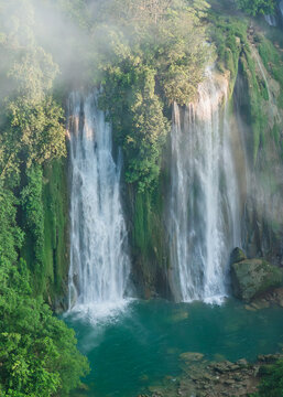 Aerial view of Cikaso Waterfall cascading down lush green cliffs into a turquoise pool surrounded by dense tropical forest in West Java, Indonesia.