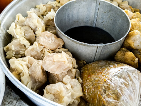 Traditional Indonesian street food assortment with siomay, batagor, meatballs, tofu, and peanut sauce served in a metal steamer at a local food stall.