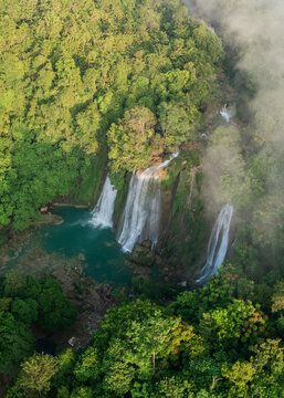 Aerial view of Cikaso Waterfall surrounded by dense tropical forest and mist in West Java, Indonesia.