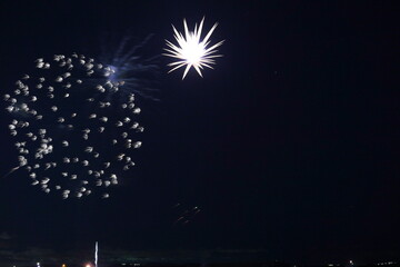 Fototapeta premium 夜空に広がる花火の爆発と星の軌跡。都市の灯りが遠くに点在する夜景。