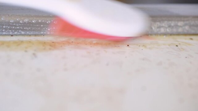 Closeup kitchen countertop grout cleaning with toothbrush, homeowner scrubs yellowed caulk near sink using foamy detergent and pinkbristled brush stubborn grime lifts revealing
