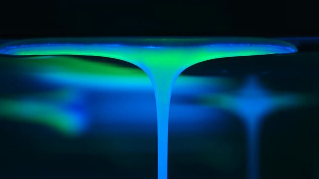Glossy liquid column drawn from upper membrane into continuous neon cyan and emerald stream over dark background, showing viscous motion, elongated shape, glowing highlights, and smooth reflective
