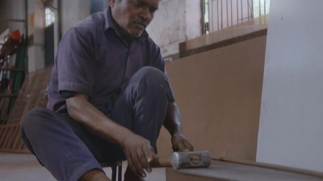An indoor close-up shot of a skilled Indian Asian male worker or craftsman sitting, checking alignment and striking the hammer with precision to straighten and correct the shape of the metal rod.