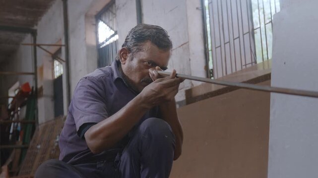An indoor close-up shot of a skilled Indian Asian male worker or craftsman sitting, checking alignment and striking the hammer with precision to straighten and correct the shape of the metal rod