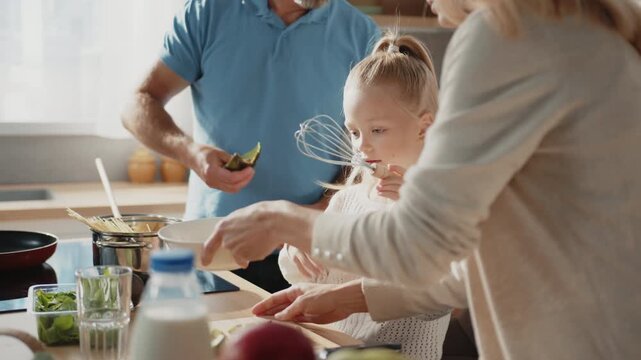 Girl with ponytail beating egg in kitchen. Family cooking together. Various vegetables on table. Children enjoying cooking food at home. Weekends. Homemade food. Vegetarian, healthy lifestyle, eco