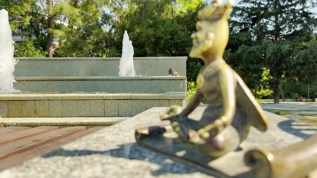 A serene bee figurine sits in a yoga pose on a stone ledge in a park in Simferopol, Crimea. The cute statue inspires a peaceful sense of calm relaxation. A sunny fountain flows softly behind it.