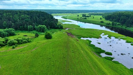 Obraz premium Green expanses of grassy wetlands in summer with winding river and forested hills in background
