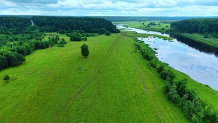 Obraz premium Aerial view showcasing lush green grasslands and riverbanks under cloudy skies in a serene landscape