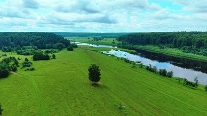 Obraz premium Aerial view of lush green fields and calm river under cloudy sky in summer landscape