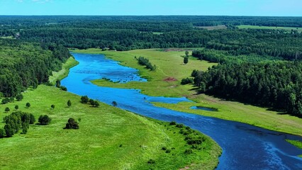 Obraz premium Meandering river flowing through vibrant green fields under a bright blue sky landscape