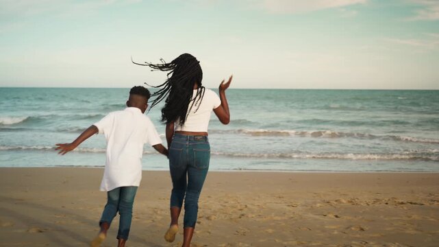 African American mother laughing and playing with son on sandy beach. Concept of motherhood, unconditional love, parenting, family happiness, outdoor lifestyle, and summer vacation
