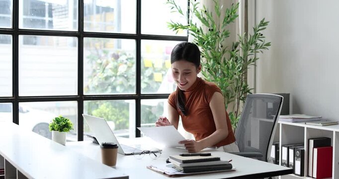 Asian businesswoman smiling and typing on laptop, happily working from a modern home office, staying connected and productive with technology for success