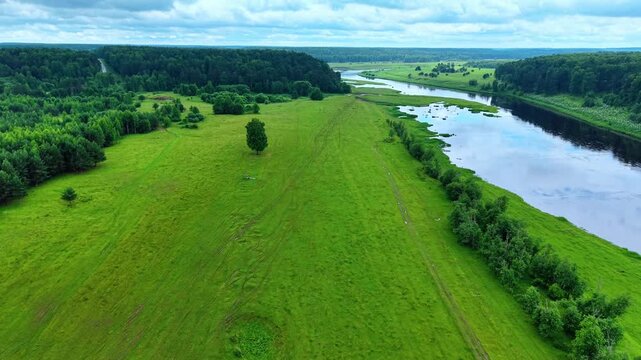 Green grassland terrain adjacent to flowing river surrounded by dense forest vegetation