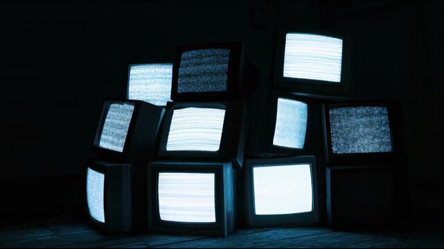 Stack of vintage retro televisions with static screens in dark room