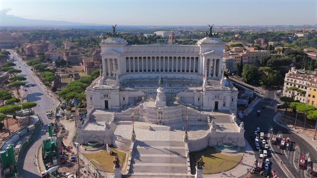 Aerial drone shot in Rome at Piazza Venezia showcasing majestic Altare della Patria monument. White marble architecture with Corinthian columns and bronze quadriga statues dominates historic.