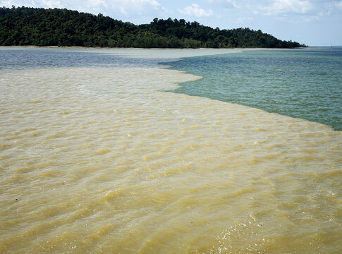 Serpentine water boundary line of muddy river silt meeting ocean water.