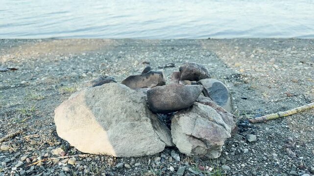Large grey stones form a rustic fire pit on a pebbled beach. The gentle water creates a peaceful feeling of solitude. This quiet scene captures the simple joy of outdoor living.