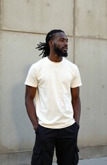 Obraz premium Young black man with dreadlocks hairstyle wears white t-shirt and black cargo pants. He stands casually with hands in pockets against a concrete wall. Confident male model looks to the side.