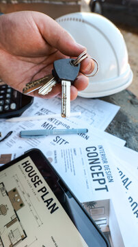 Holding keys to a new home with architectural plans and hard hat nearby