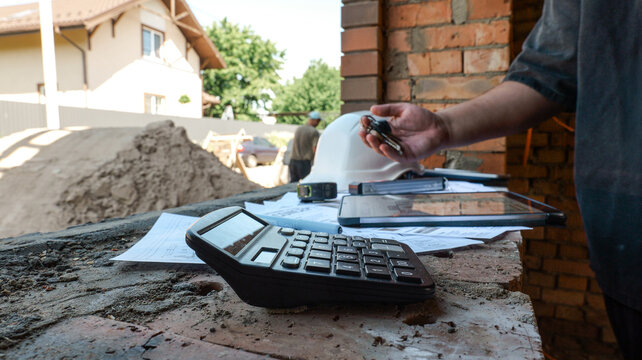 Construction site manager reviewing plans and using calculator with keys in hand