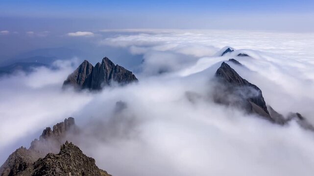 Aerial slow pan tracking motion of mountain peaks emerging through rolling clouds over alpine ridge at high elevation morning daylight