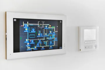 A smart home automation system is mounted on white wall, displaying digital floor plan with various controls, closeup © Alex Tihonov