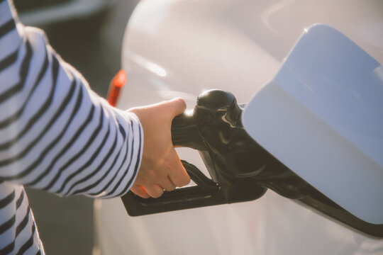 Close-up of a hand refueling a car with a green gas pump nozzle. Fueling a vehicle at a gas station. Gas pump, refueling, and car fueling process.