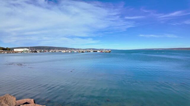 Slow motion footage of Digby Harbour and the Bay of Fundy in Digby Nova Scotia Canada showing calm blue coastal water distant boats harbour walls and a wide open sky with soft sweeping clouds