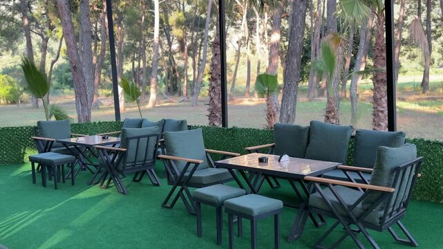 Outdoor restaurant seating area surrounded by lush trees and greenery. Garden dining, hospitality, caf&eacute; terrace, relaxation, leisure and nature-inspired dining concept.