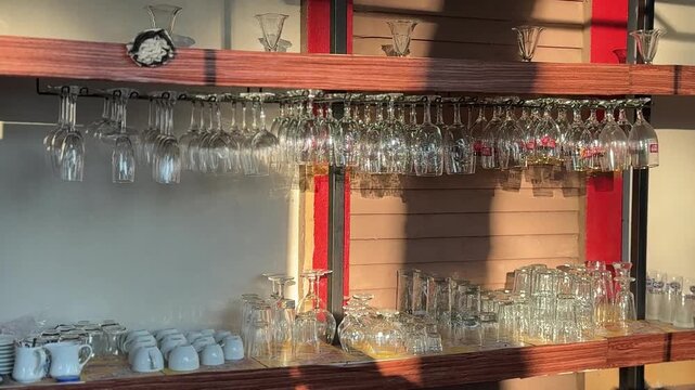 Bar shelves with neatly arranged hanging wine glasses and cups in warm ambient lighting. Hospitality, restaurant interior, beverage service, dining and bar equipment concept.