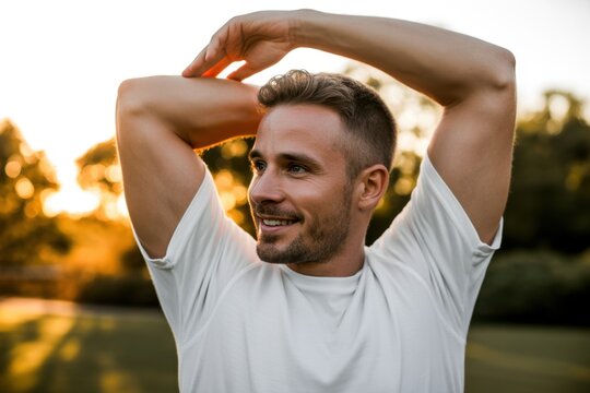 Athletic young man stretching his arms and shoulders outdoors during a golden hour workout session in a park, focusing on fitness, healthy lifestyle, and active movement