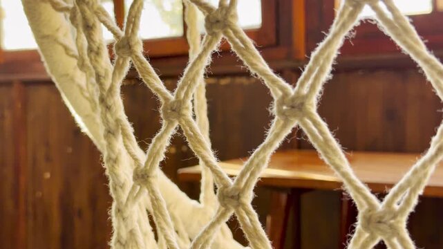 A soft cotton macrame net creates a cozy, rustic feel in a sunlit room. Its intricate woven knots evoke a sense of calm and nostalgic comfort against the warm wooden background.