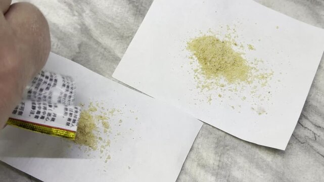 A hand carefully pours out yellow insect bait granules onto small white papers. This precise preparation brings a feeling of comfort, control, and cleanliness to the home.