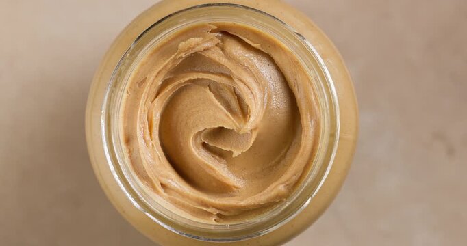 Open Jar of Peanut Butter Rotating on Warm Beige Background, Top View