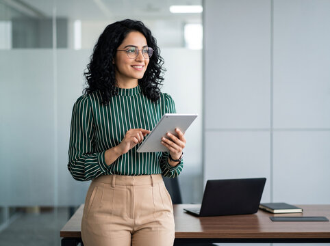 confident young Indian businesswoman holding tablet in modern office with copy space for leadership and corporate advertising